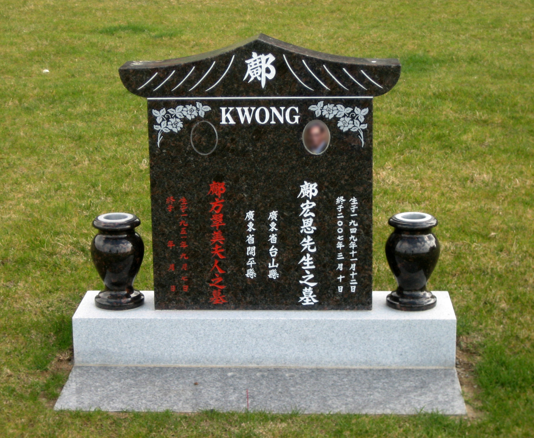 Black tombstone with white and red engravings and incense holders on either side
